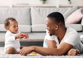 Shared Parental Leave. Young Black Father Playing With Little Baby At Home, Happy African American Man Spending Time With His Adorable Infant Child In Living Room, Enjoying Fatherhood, Copy Space