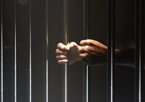 This image captures the gripping despair of incarceration with a close-up of hands clutching the cold, unforgiving metal bars of a jail cell, symbolizing loss of freedom.